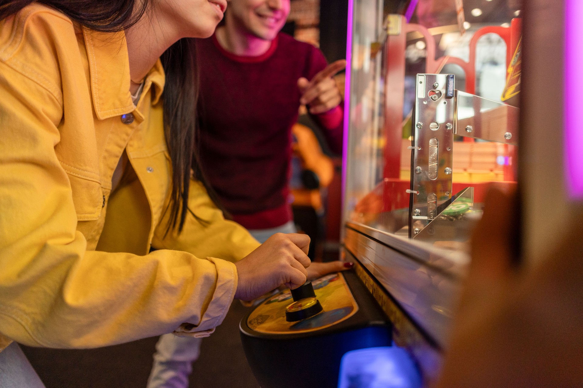 Friends Playing Claw Machine at Arcade. Close-up view of two friends concentrating on operating a claw machine in a lively arcade setting.